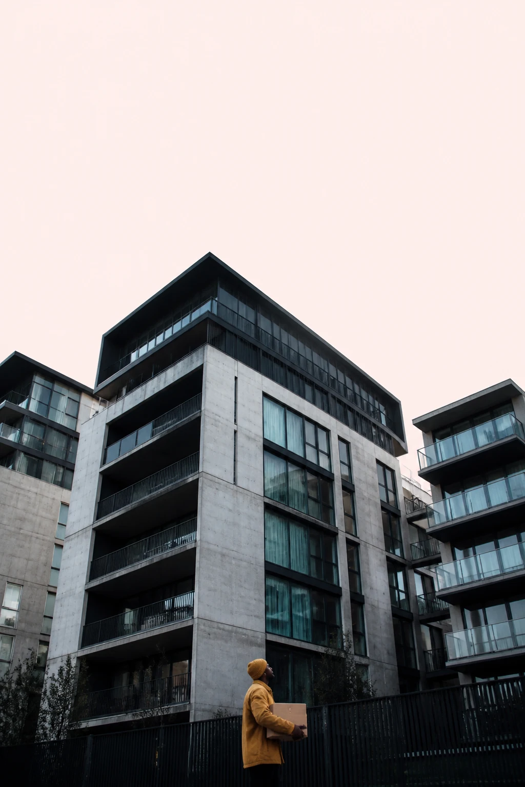 Modern multi-storey building with large windows, balconies and green spaces on the roofs and railings.